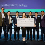 One older man standing next to 6 students in business attire holding novelty check for $15,000.