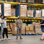 Image of four male students listening to a volunteer in a warehouse.