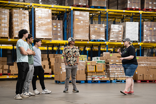 Image of four male students listening to a volunteer in a warehouse.
