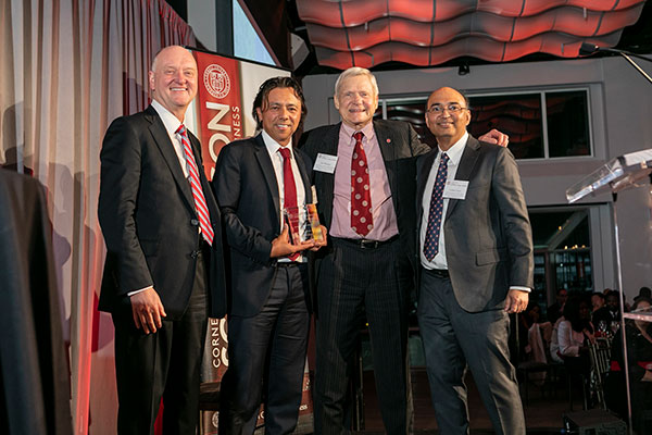 Four men standing side by side, arms around shoulders, and smiling. One is holding a crystal award.