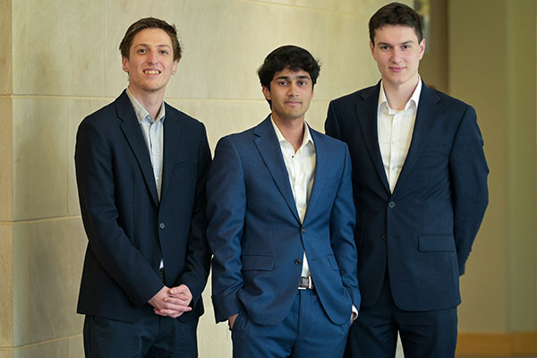 Three men dressed in business attire standing side by side and smiling at the camera.