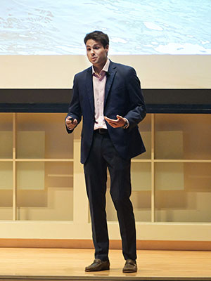 a man dressed in busines attire standing on a stage and speaking.