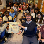 Image of a large group of students gathered together with a Cornell banner during the Rummo-Cornell Family Business Trek