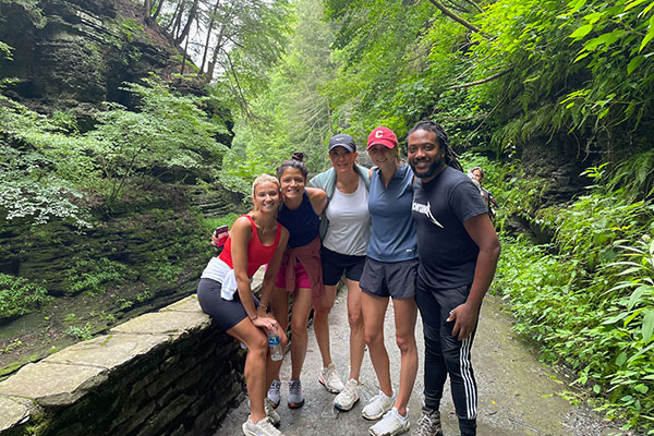 4 women and 1 man standing on a path next to a rock wall in a green, woodsy gorge.