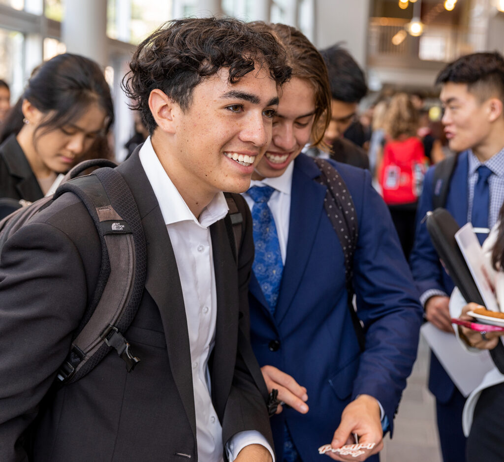 Two male students in business attire smile during a busy student clubs event.