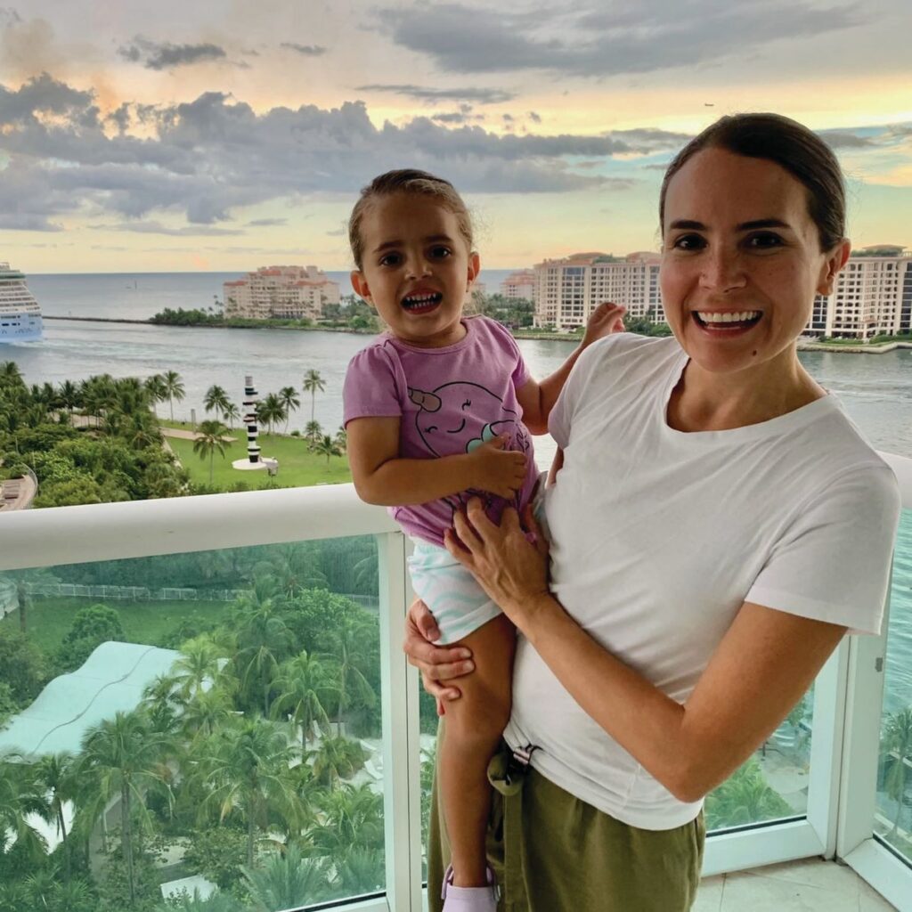 Gilda poses on a balcony overlooking water holding her daughter.