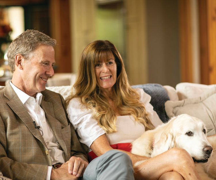 Peter and Stephanie Nolan sit on their couch with one of their dogs sitting on Stephanie's lap.