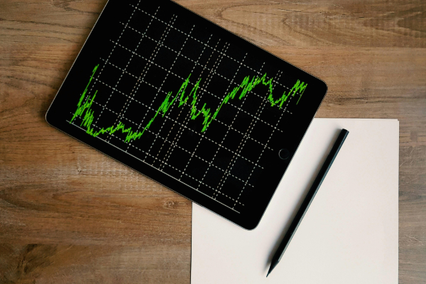 Image of a digital device displaying market activity with a pad of paper and a pen