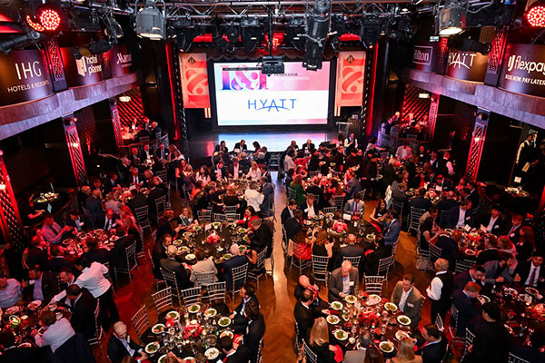 Photo taken from above of a large banquet hall filled with tables and people with a stage at the front of the room.