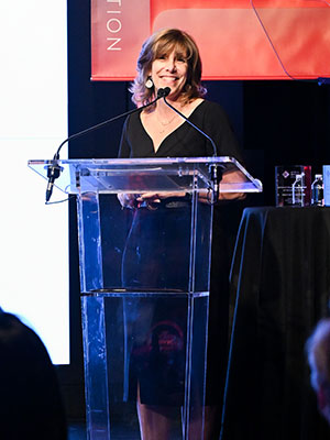 A woman standing at a podium on stage and speaking into a microphone.