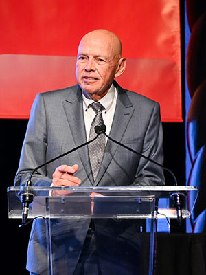 a man standing at a podium on stage and speaking into a microphone