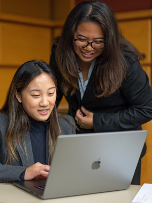 Two female MBA students working together on laptop during crisis challenge competition