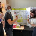 Jennifer White-Phalen and Miwako Nara Uemura stand in front of their project’s poster. Hammerstone founder Maria Klemperer-Johnson has carpentry tools in hand.