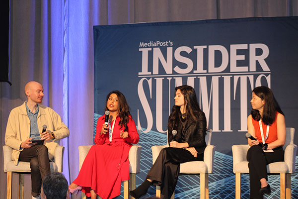 A moderator and three panelists, all with microphones, seated on stage.