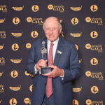 George Gellert in front of a background holding his award