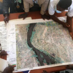 A group of people crowd around at a map with a river, the photo is taken from above.