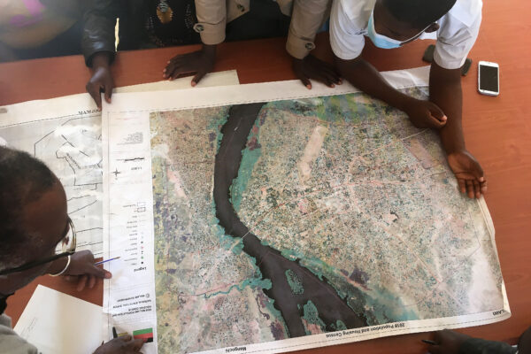 A group of people crowd around at a map with a river, the photo is taken from above.