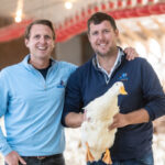 Two men, one holding a large white duck, smile.