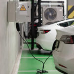 Two white electric cars at a charging station in a green-painted parking garage.