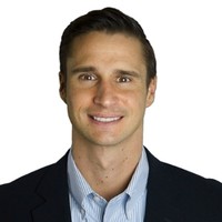 Professional headshot of Austin Blais smiling and standing in front of a white background.