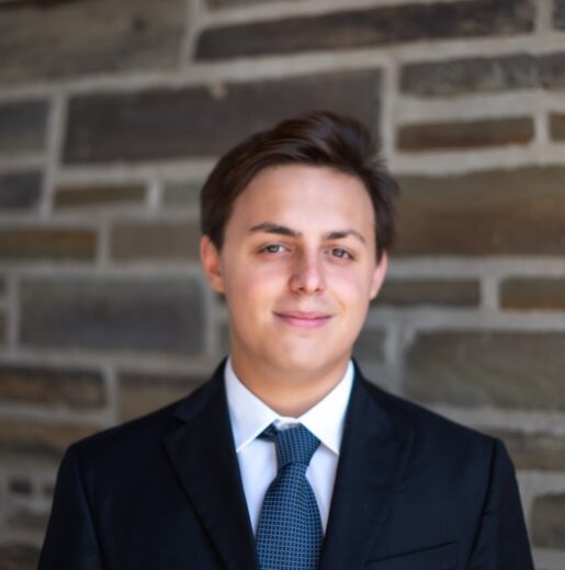 Man standing in front of a brick wall with a suit and tie on.