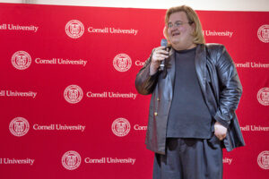 a person with a microphone stands in front of a red background.