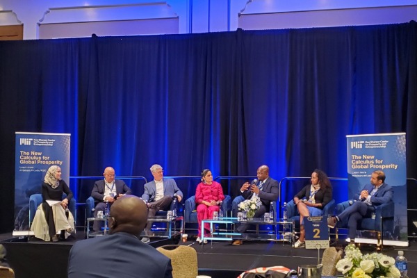 Panel of seven speakers seated on stage with banners.