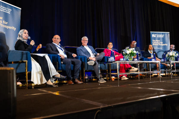 Panel of six speakers seated on stage with banners.