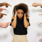 A young, frustrated woman with several hands pointing their fingers at her