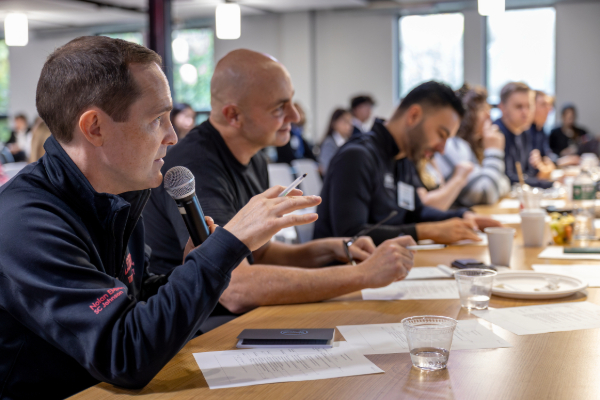 multiple people sit on one side of a table, and the man closest speaks into a microphone.
