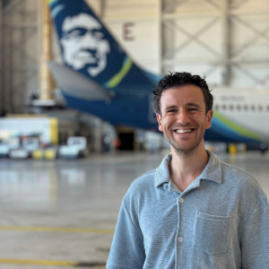 Alex Levy stands in an airplane hanger with a plane visible in the background.