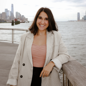 Alice Navadeh leans on a railing next to water with a cityscape in the background.