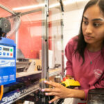 A woman leans in to work with a piece of equipment.