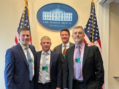 Text: Rob and three other LevelTen executive members smiling in front of a White House sign and two American flags