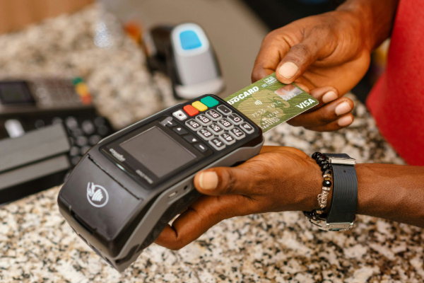 A person inserts a green Visa debit card into a black point-of-sale terminal on a granite countertop.