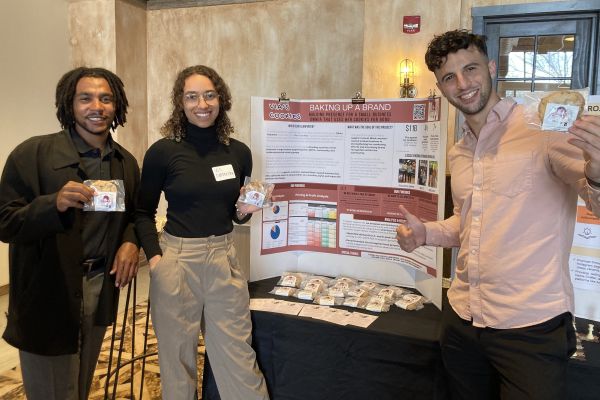 Two MBA students standing in front of their project poster with the founder of Via’s Cookies