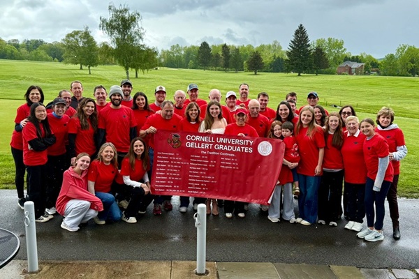 The Gellert family wears matching red t-shirts and poses with a Gellert family Cornell graduates banner. 