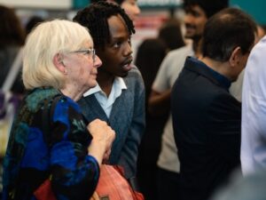 A young man explains his poster to an older woman, who is attending his poster session.