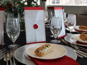 An appetizer sits on a white plate and red napkin, a wax-sealed menu standing up behind it.