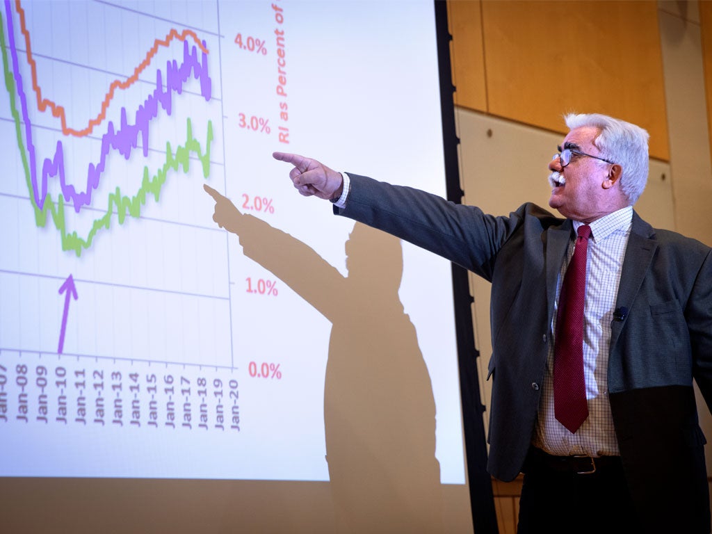 Professor points at screen displaying a chart during a presentation.