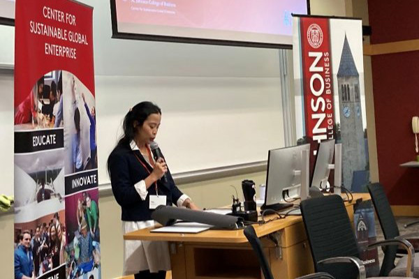 Tika Diagnestya using a microphone to present with a whiteboard as her backdrop.