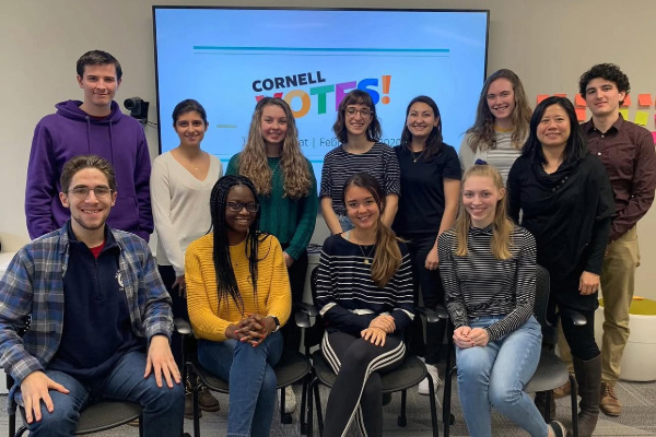 Twelve undergraduate students standing in front of a sign that reads “Cornell Votes!”