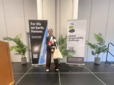 Tika Diagnestya smiling on stage with Global Sustainability Challenge signage behind her.