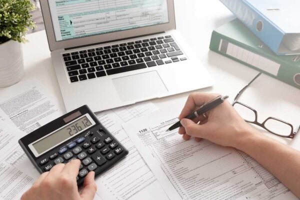 A person filling out a form with their computer and a calculator