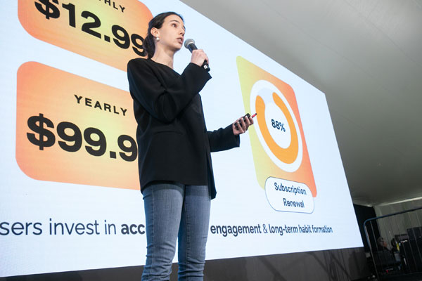 Cornell student presenting at a pitch competition, holding a microphone in front of a slide showing subscription pricing and an 88% renewal rate