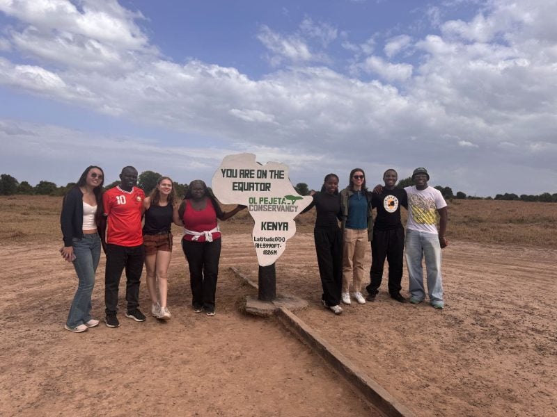 Students pose in front of a sign that says "You are on the Equator" in Kenya
