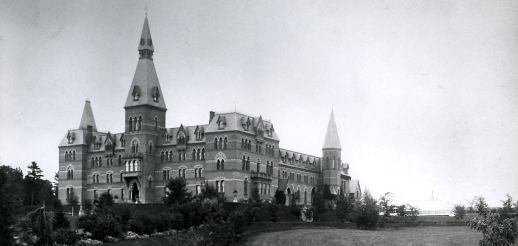 A black and white photo of Sage Hall, a brick building with a tall spire, against the sky
