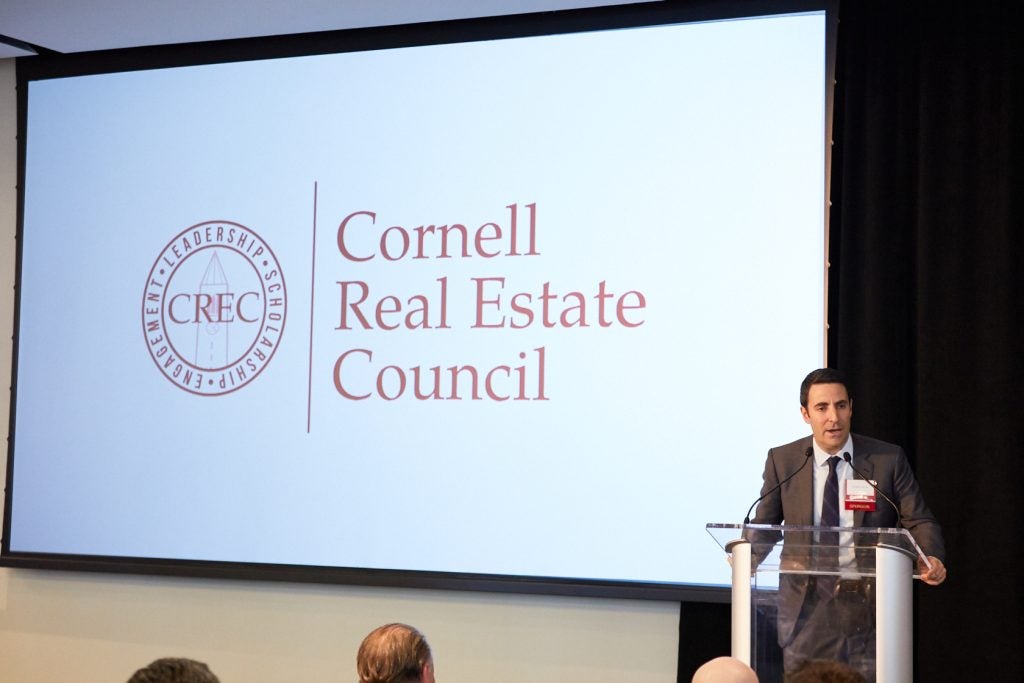 Speaker presenting at CREC event to a group of members with a projector behind him displaying the organization's logo. 