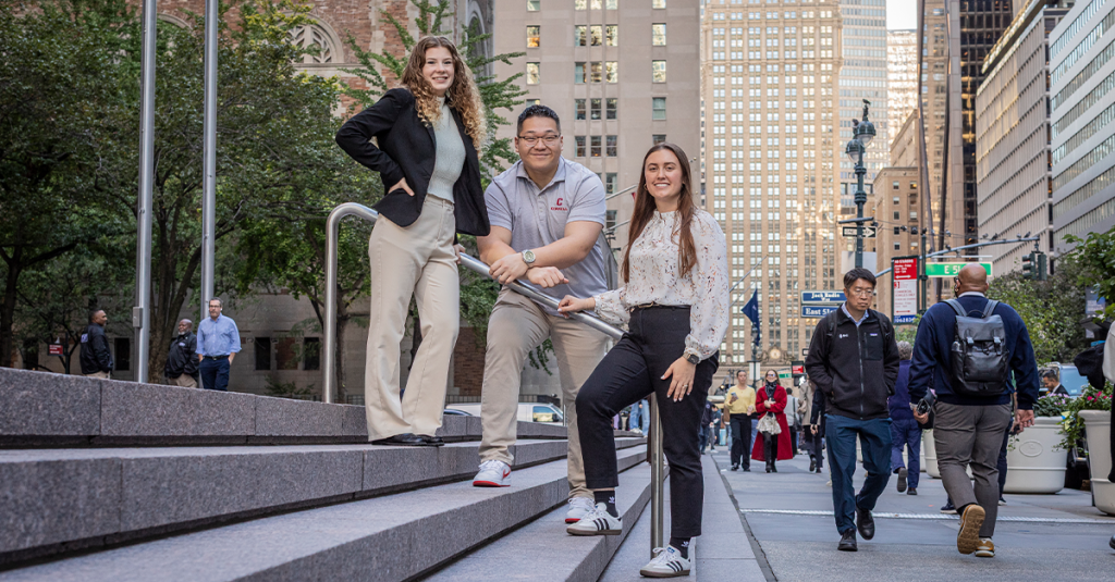 Three Cornell Master's in Real Estate students stand outside on the steps leading into a building next to a busy NYC street.