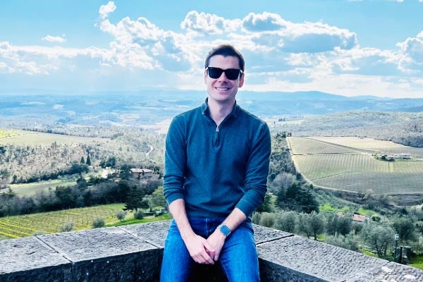 Louis Guzzo, MPS '23 sits on a wall overlooking the Italian countryside.